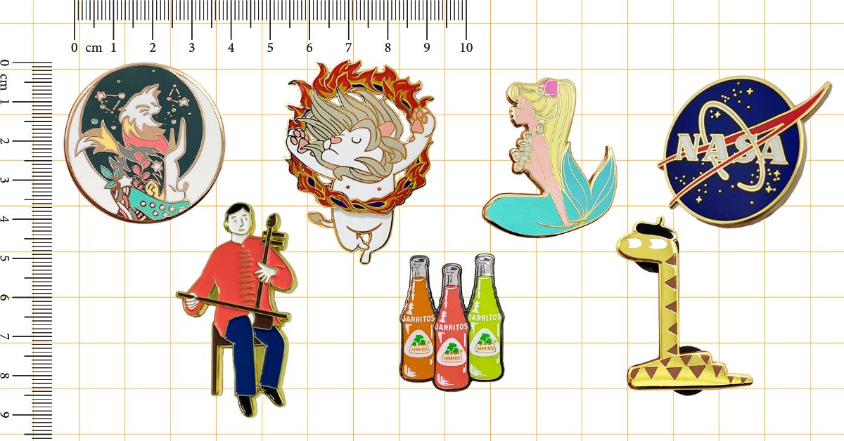 A collection of custom enamel pins with diverse designs, including characters and logos, displayed on a grid with a ruler for size reference.