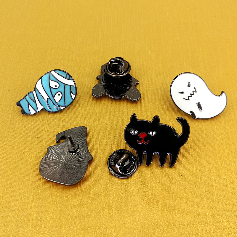 A collection of Halloween-themed enamel pins with various backings, including a mummy, ghost, and black cat.