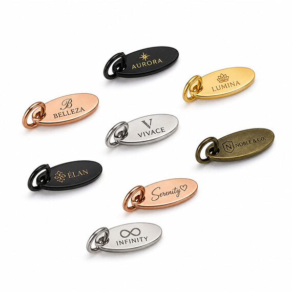 Oval custom logo jewelry tags with metal jump rings in gold, silver, rose gold, black, and antique finishes, engraved with varied brand designs.