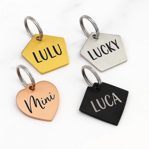 A flat-lay photograph displays five custom engraved pentagon, heart, and diamond shaped pet ID tags with laser-etched names including Lulu and Lucky on brushed metal surfaces.