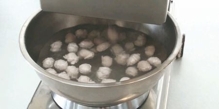 A rotating platform with a bowl containing water collects meat balls to prevent them from sticking.