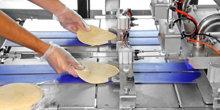 Тортильи ручным образом помещаются на конвейер