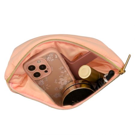 Top view of a peach quilted makeup bag with gold zipper, opened to show spacious interior holding cosmetics and a smartphone.