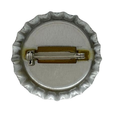 A traditional safety pin attached to the back of the bottle cap pin that allows it to be fastened to clothing or accessories.