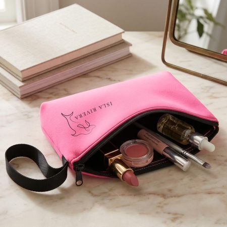 Custom pink neoprene toiletry bag with wrist strap, partially open showing makeup items inside on vanity table
