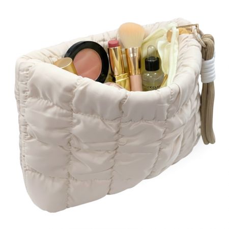Открытая кремовая стеганая косметичка, наполненная косметикой, с просторным внутренним отсеком для косметических средств.