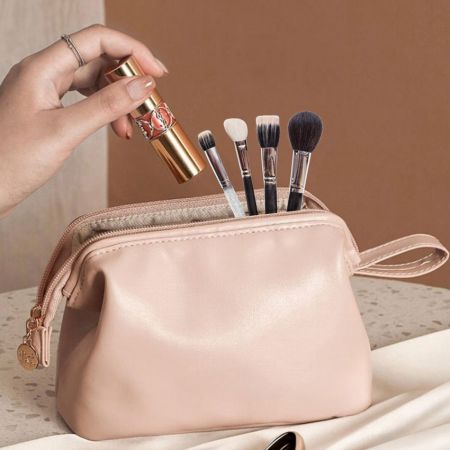 Leather cosmetic bag with makeup brushes inside and a hand holding a lipstick