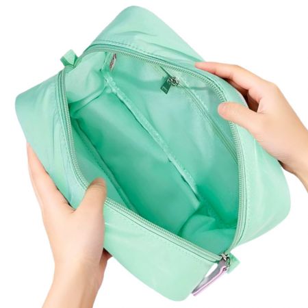 Вид сверху на пухлую косметичку мятного цвета с отстегивающимся верхом, показывающую просторное основное отделение с соответствующим внутренним карманом на молнии