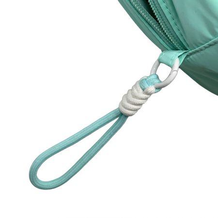 Крупный план пухлой косметички мятного цвета с заплетенным ремешком на запястье, прикрепленным к металлическому кольцу