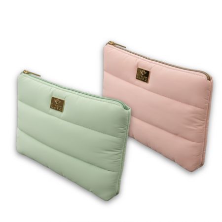 Twee pastelgeklede cosmetica tassen in mintgroen en lichtroze met metalen logo platen en een bovenste ritssluiting.