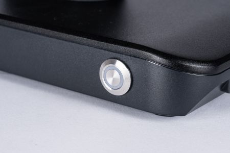 Kovové tlačítko napájení s modrým LED podsvícením při zapnutí.