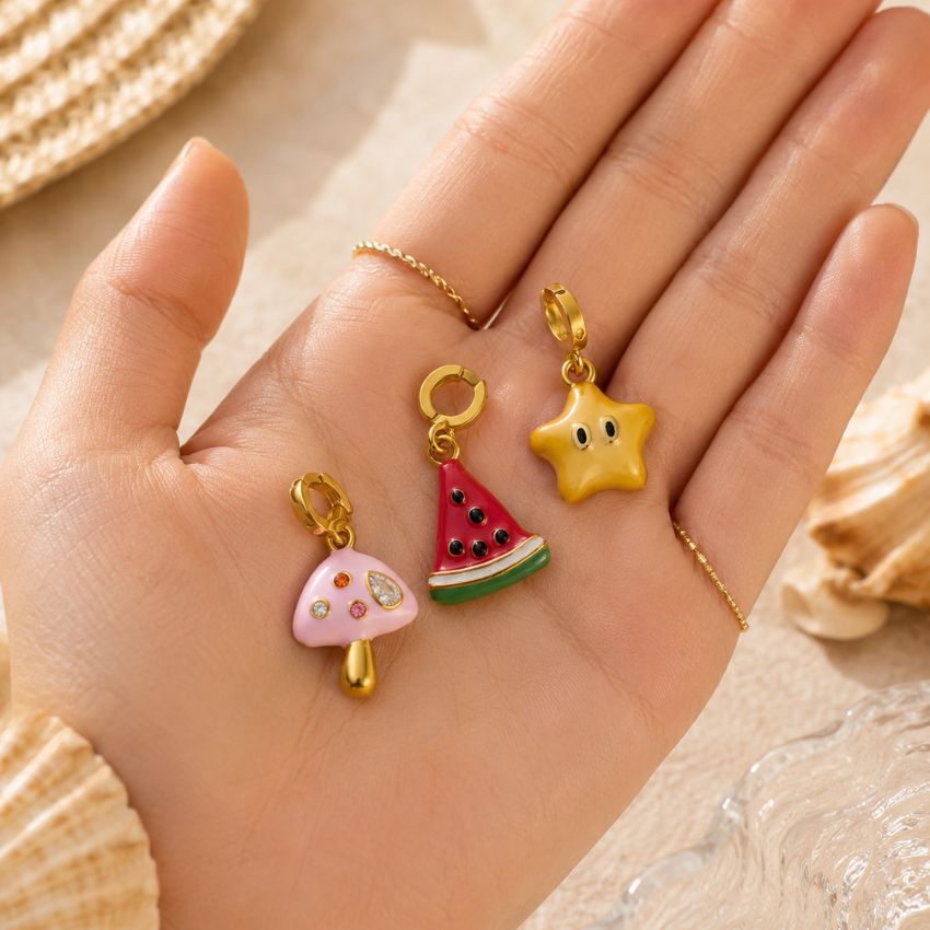 Encantos de esmalte de hongo, sandía y estrella sostenidos en una mano, mostrando la fabricación de joyería al por mayor personalizada.