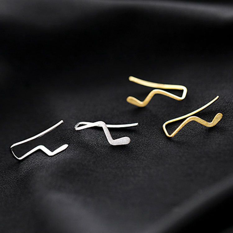 Una collezione di orecchini a perno semplici a onda in argento sterling 925, sia in finitura argento che oro, esposti su una superficie scura.