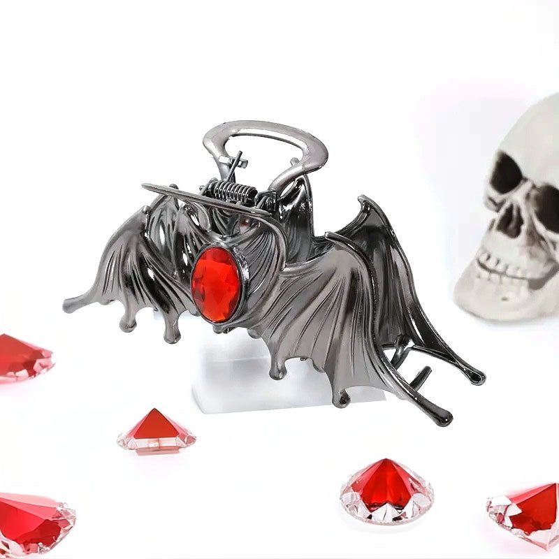 Un primo piano di un fermaglio per capelli di Halloween a forma di pipistrello nero con una gemma rossa sorprendente al centro, che mostra il suo design metallico dettagliato.