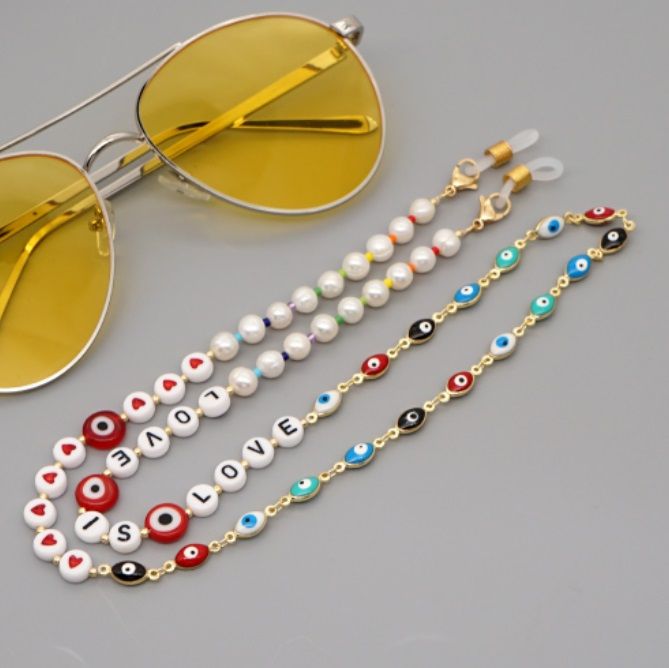 En stilren guldpläterad Evil Eye pärlad kedja som visas fäst vid ett par solglasögon, som fungerar som en modeaccessoar för glasögon.