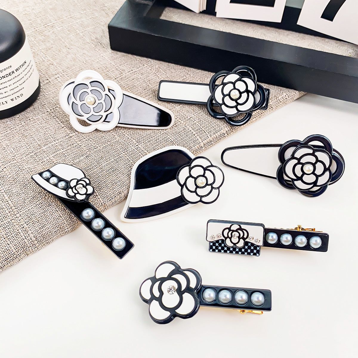 Una collezione di eleganti clip per capelli acriliche bianche e nere con vari design di fiori di camelia e perle, esposte su uno sfondo neutro.