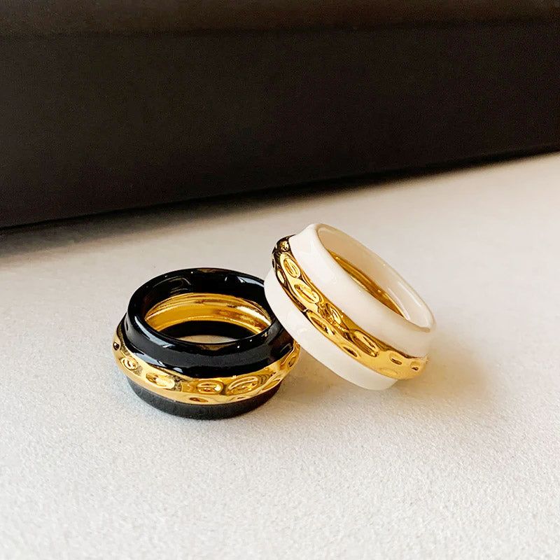 A set of vintage-style brass rings with double-color enamel, one in black and gold, the other in white and gold, displayed side-by-side.