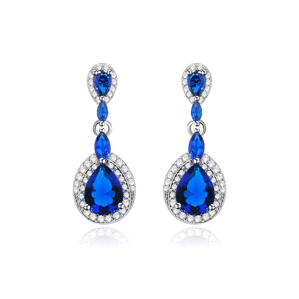 Boucles d'oreilles pendantes en forme de poire avec des verres en saphir bleu et des zirconiums cubiques blancs dans un cadre plaqué rhodium, présentées sur un fond blanc.