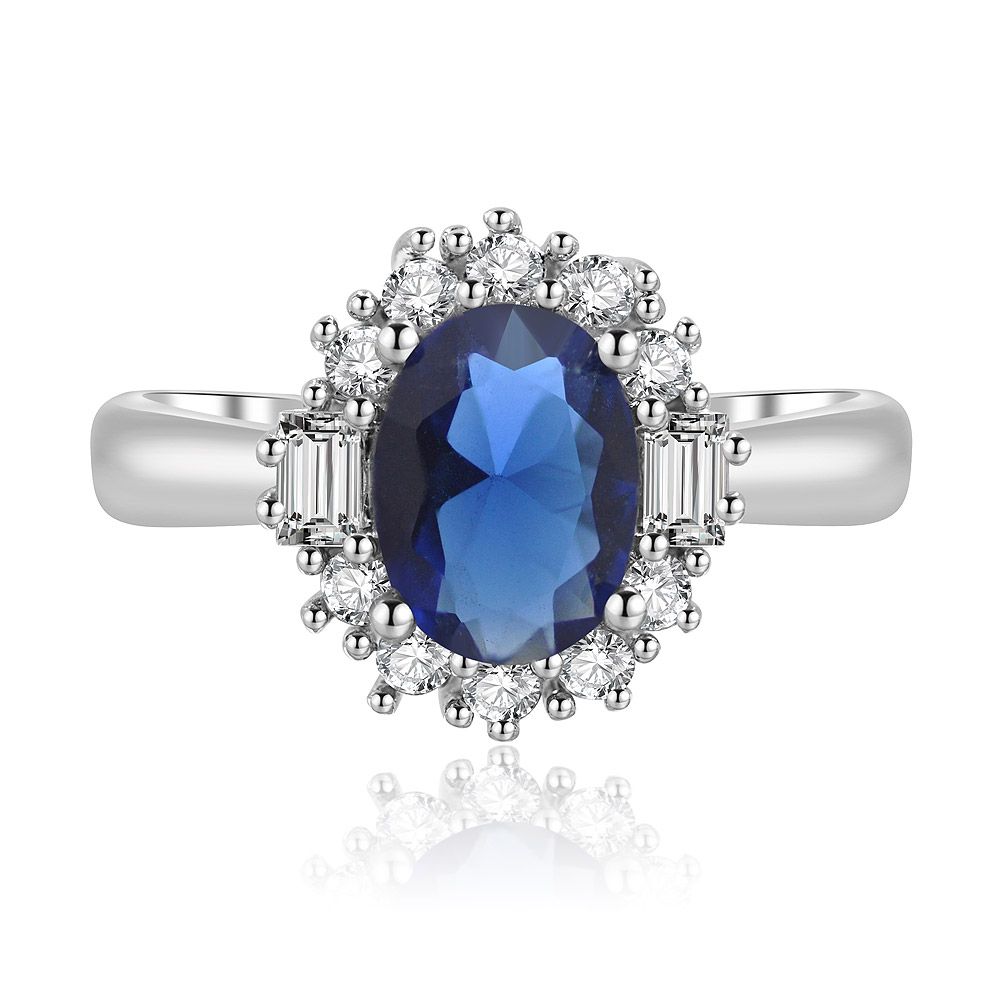 Frontalansicht des einzelnen ovalen Saphir-Zirkonia-Rings, der den strahlend blauen Mittelstein und den funkelnden Zirkonia-Halo auf einem rhodiumbeschichteten Band präsentiert.