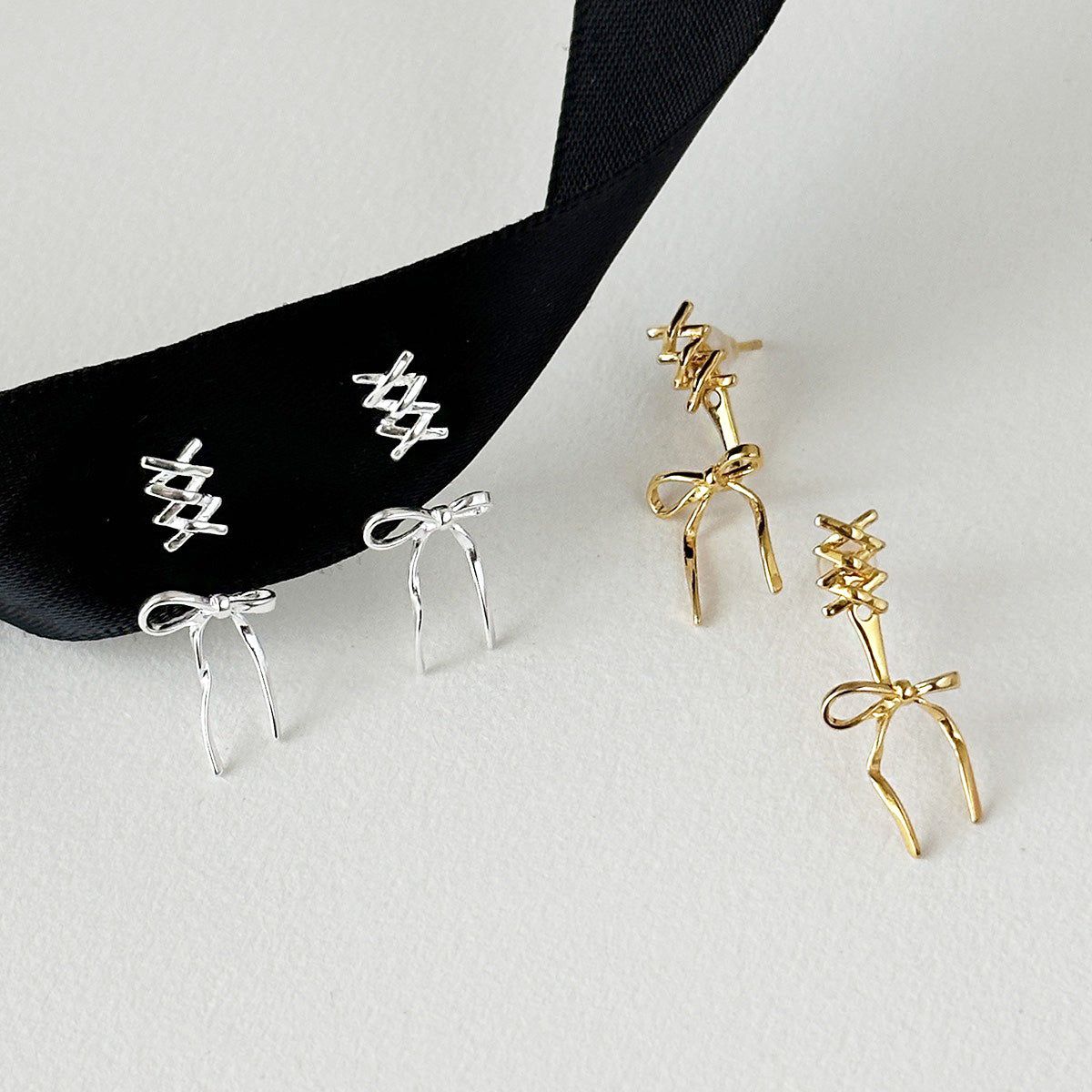 Ett par silver och ett par guld 925 sterling silver balettband båge-studörhängen visade på en vit bakgrund, vilket framhäver den eleganta designen för grossist.