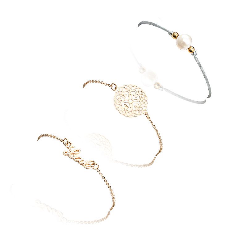 Una collezione di tre bracciali impilabili Love Pearl, realizzati in ottone placcato oro, perle e ciondoli unici, esposti su uno sfondo bianco.