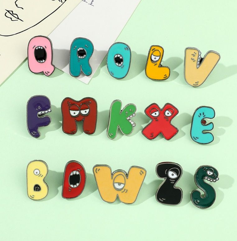 A vibrant collection of wholesale colorful letter A-Z brooch metal lapel pins, each featuring a unique cartoon expression. Customizable enamel pins by JR Fashion Accessories.