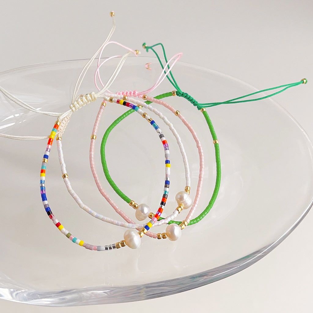 Un'artistica disposizione di braccialetti intrecciati a mano con perline di riso bohemien colorate e perle, esposti su un piatto di vetro, che mostrano la varietà del set.