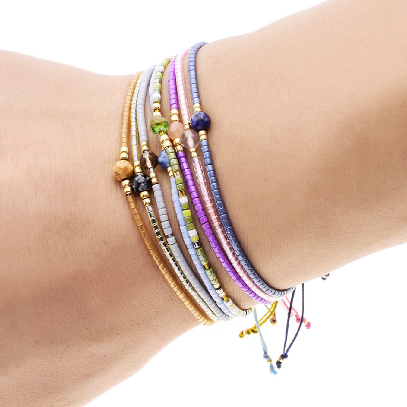 Una pila di braccialetti bohemien intrecciati a mano multicolore con piccole perline di riso e pietre naturali, indossati su un polso.