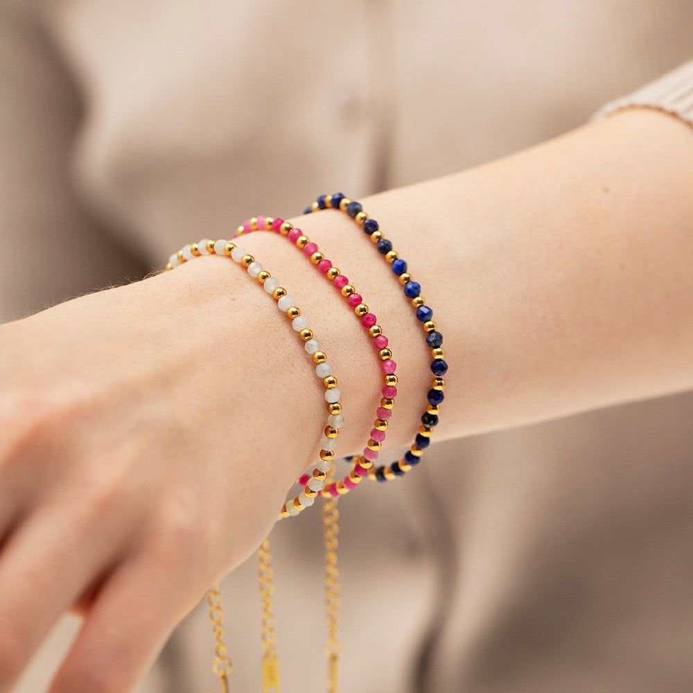 A close-up of a wrist adorned with a set of five stainless steel stacking bracelets featuring colorful glass beads in various designs.