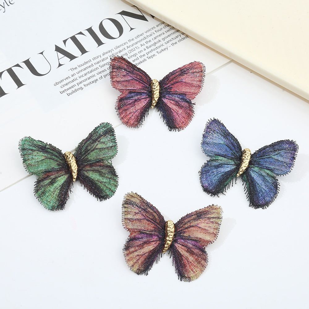 Um conjunto de quatro broches de borboleta vintage bordados em gradiente nas cores azul, verde, rosa e multicolorido, exibindo bordados detalhados nas asas e corpos de ouro.