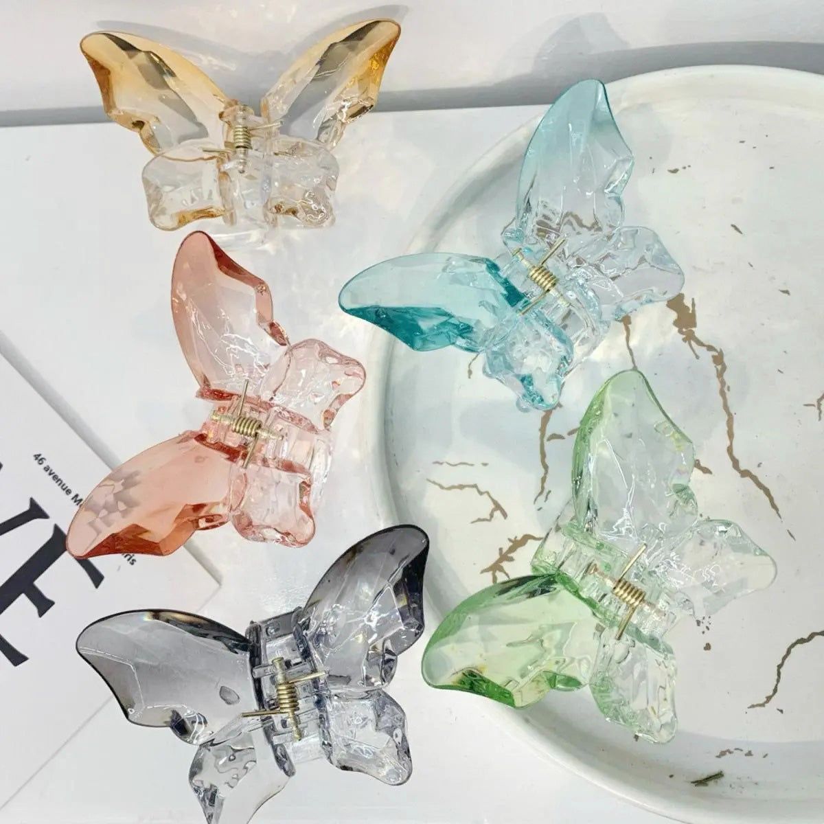 Una collezione vivace di clip per capelli a forma di farfalla colorate in varie finiture opache e trasparenti, disposte ordinatamente per la visualizzazione.