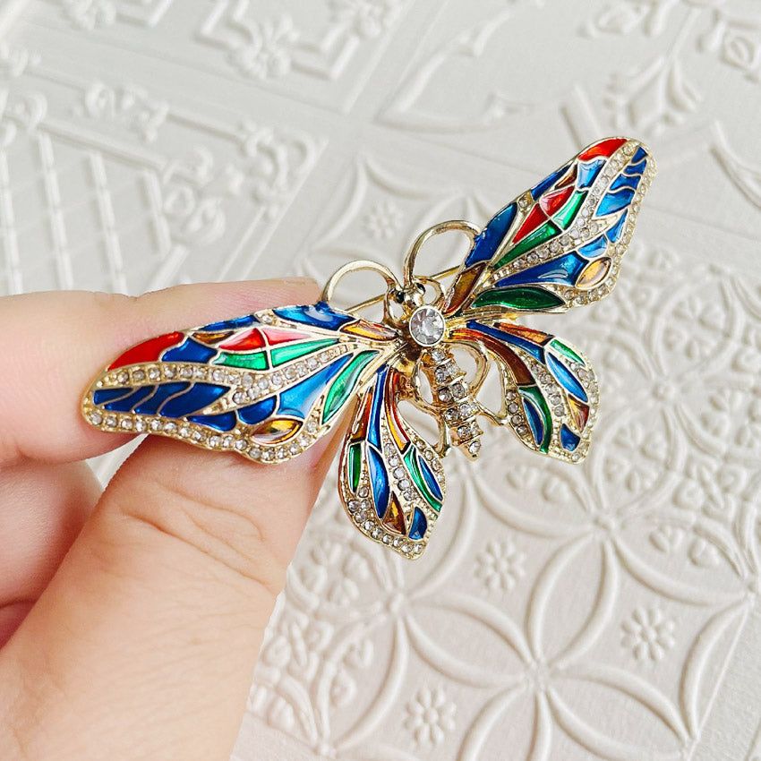 Una splendida spilla a forma di farfalla placcata in oro con ali smaltate multicolori e dettagli di strass scintillanti, che mostra un design di moda retrò.