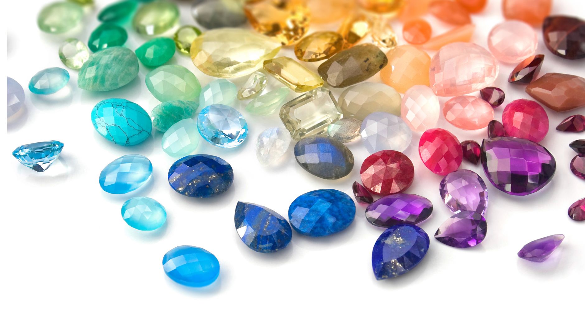A vibrant rainbow arrangement of various colorful gemstones, representing the different monthly birthstones available for custom jewelry from JR Fashion Accessories.