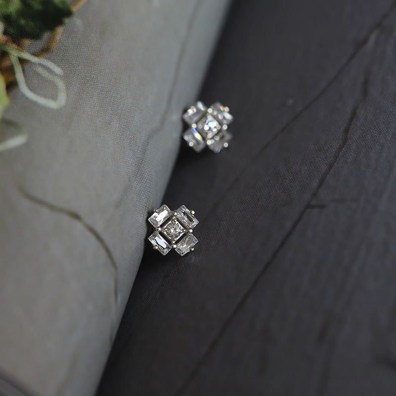 Un paio di orecchini a perno in argento sterling 925 a forma di cubo di ghiaccio con zirconia cubica, esposti su una superficie in legno scuro.