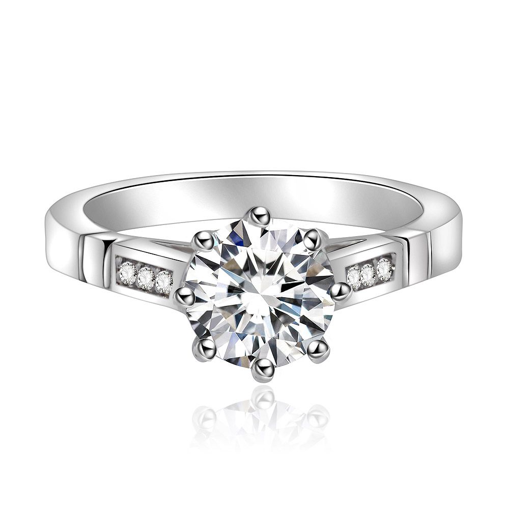 Un primo piano dell'Anello Bianco Rotondo con spalla, che mette in mostra la sua pietra centrale rotonda in zirconia cubica circondata da pietre più piccole su una fascia in ottone placcata in rodio.