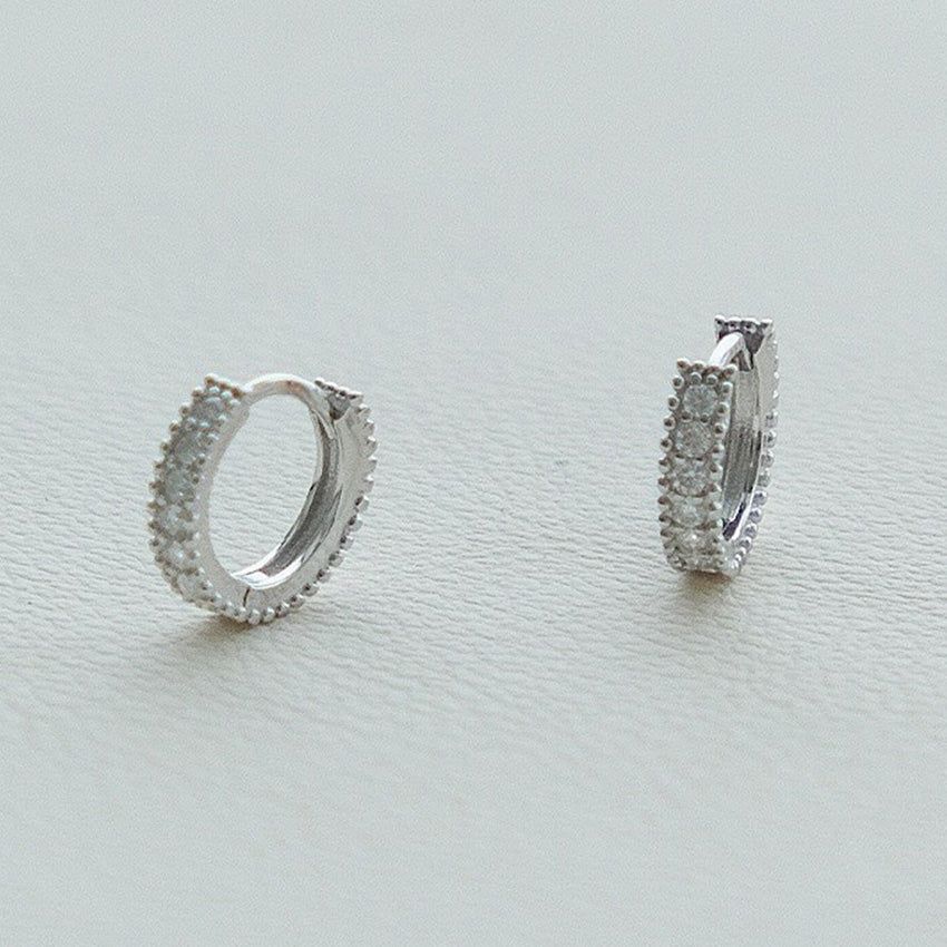 Un paio di orecchini huggie in argento sterling 925 con placcatura in platino e un'impostazione a pavé di scintillanti pietre di zirconia cubica.
