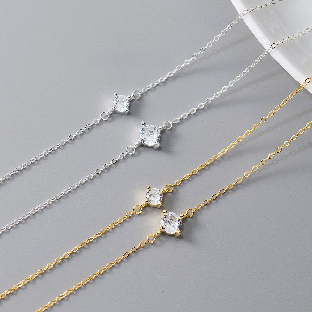 Una collezione di bracciali in argento sterling 925 con un singolo strass, esposti in finiture dorate e argentate e in due diverse dimensioni delle pietre.
