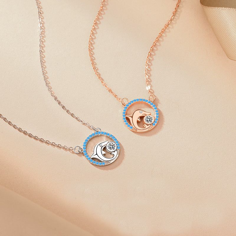 A pair of 925 sterling silver dolphin pendant necklaces, one in a silver finish and the other in rose gold, both adorned with delicate blue gemstones.