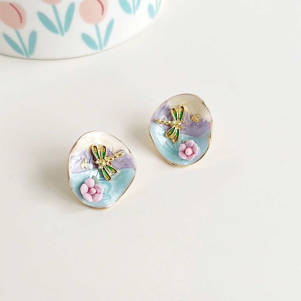 A close-up of the wholesale painting-style gold plated dragonfly stud earrings, featuring a vibrant gradient enamel finish on a brass base. The design is nature-inspired.