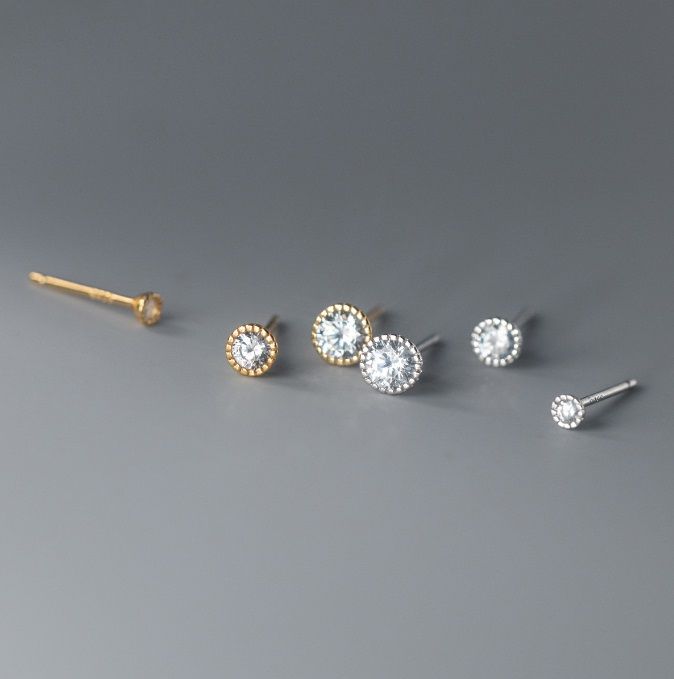 Un paio di orecchini a bottone Halo in argento sterling 925 con gemme in zirconia cubica trasparente, mostrati sia in opzioni di placcatura argento che oro.