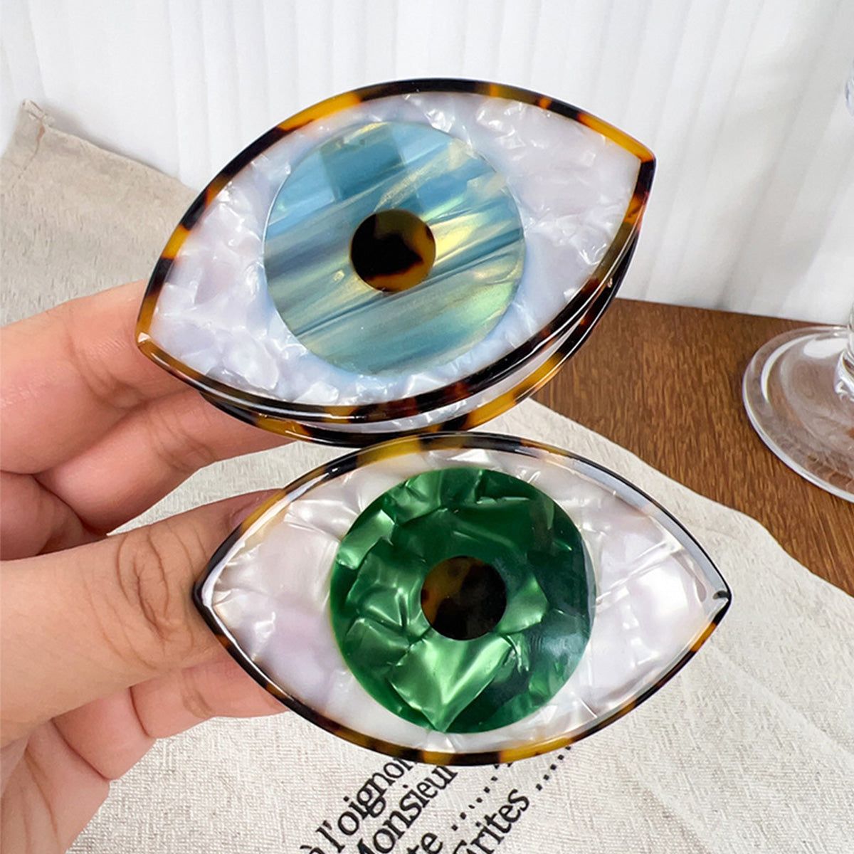 Um par de clipes de cabelo com Olho Turco em azul e verde, feitos de acetato com padrão de tartaruga, simbolizando o amuleto protetor turco.