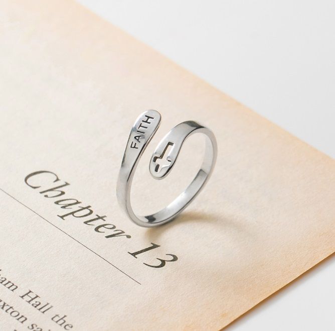 Un anello in argento sterling 925 inciso con la parola 'FEDE' e un simbolo di croce, poggiato su un libro aperto per mostrare il suo design ispiratore.