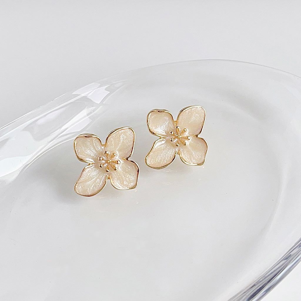 詳細な花のデザインを披露する金メッキの白いエナメルの花のスタッドピアスのペアが、白い皿の上に優雅に展示されています。