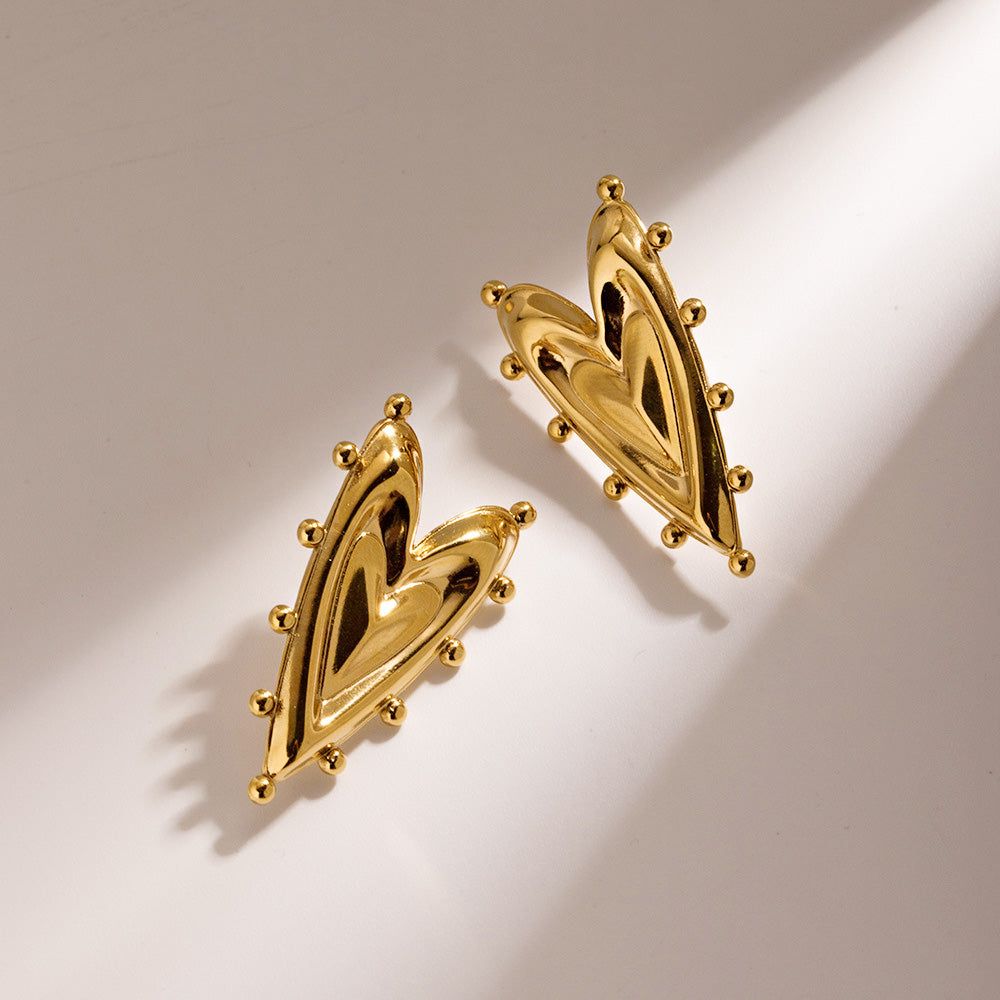 Een paar 18k vergulde roestvrijstalen stud oorbellen met een modern, abstract half-hart en bol ontwerp, weergegeven op een schone, neutrale achtergrond.