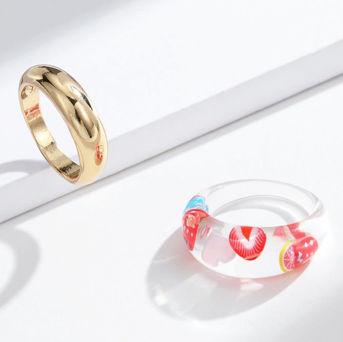 A product shot of the Fruit Acrylic and Metal Stackable Band Ring Set, featuring a clear acrylic ring with fruit designs alongside a complementary gold metal band.