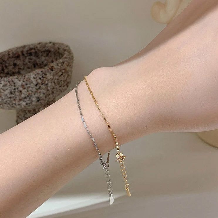 La muñeca de una modelo adornada con las pulseras de cadena de geometría cuadrada de plata esterlina 925, mostrando tanto el elegante acabado plateado como el radiante dorado.