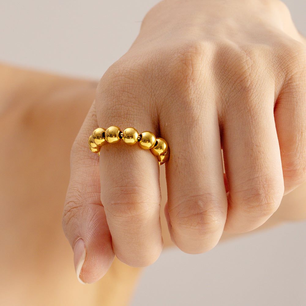 De hand van een model die de verstelbare ring van roestvrij staal met punk kralenbal in een gouden afwerking draagt, en het elegante ontwerp toont.