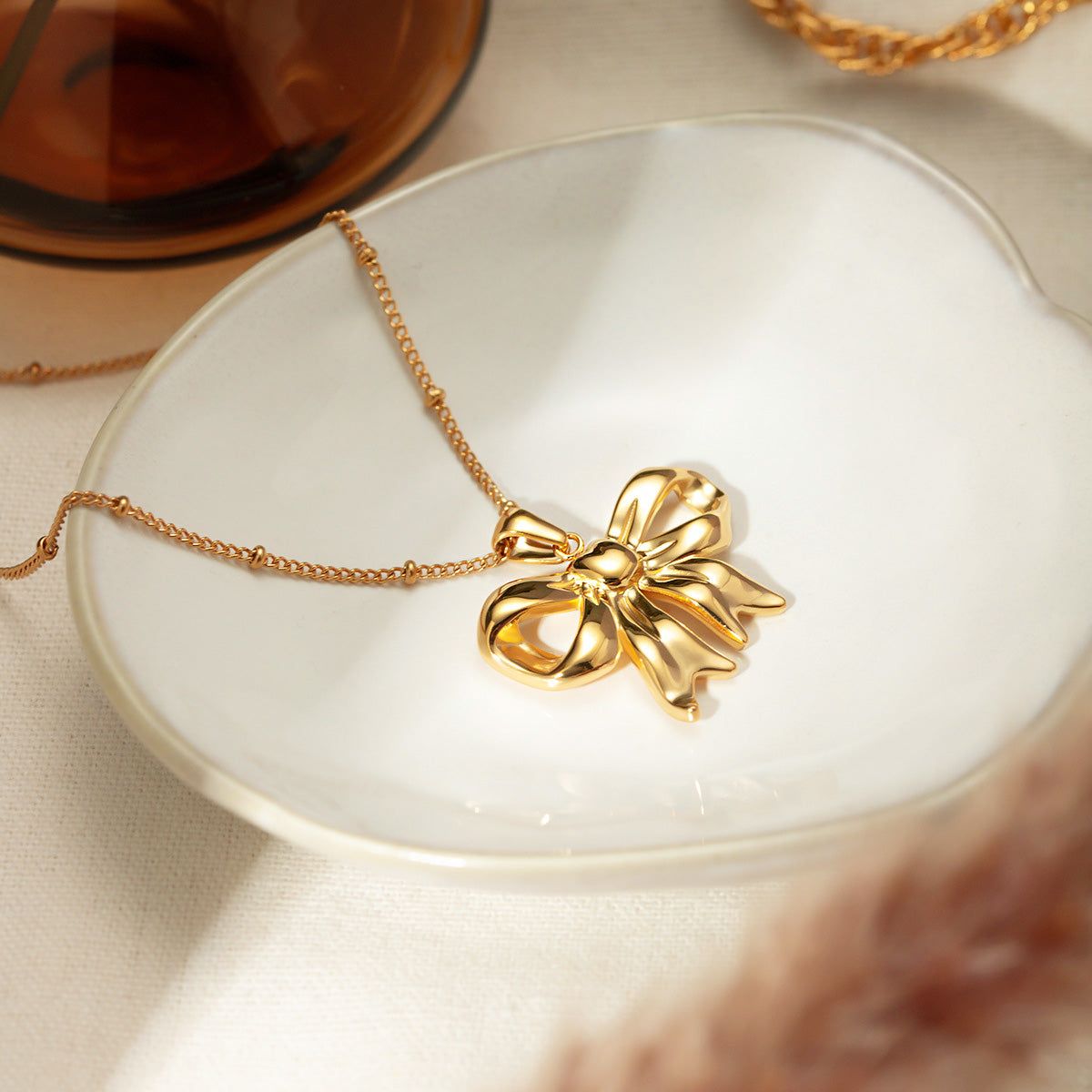 Gros plan sur un délicat collier pendentif en forme de nœud en ruban plaqué or, fabriqué en acier inoxydable, présenté sur une surface blanche propre.