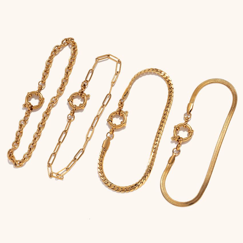 さまざまなデザインの金メッキ仕上げの女性用ステンレススチールチェーンブレスレット5点のコレクション。ペーパークリップやスネークチェーンを含み、白い背景に配置。