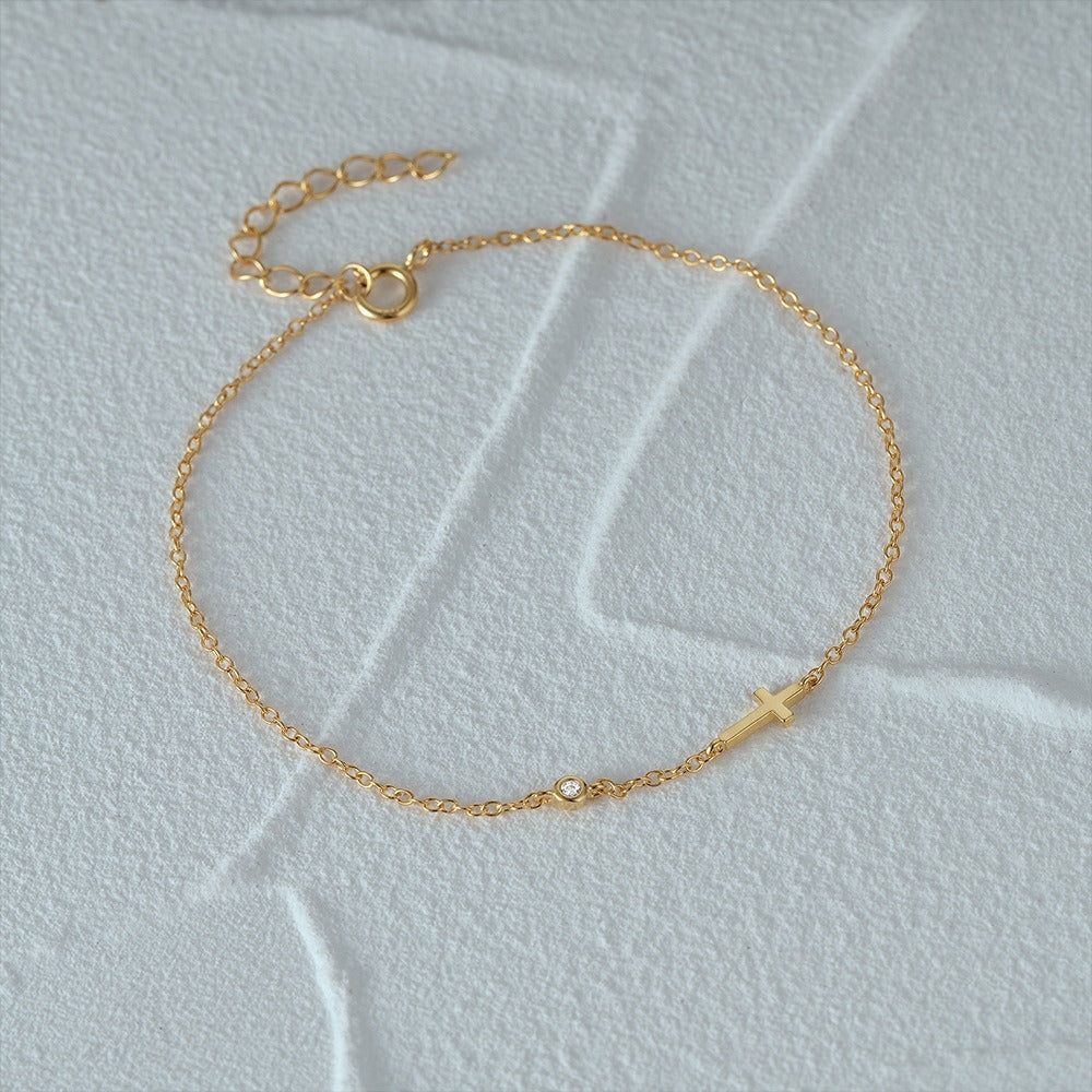 A delicate 925 sterling silver gold-tone bracelet featuring a sideways cross charm and a sparkling cubic zirconia stone on a white background.